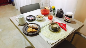 Een eettafel met een bord eten, een kan sap, een kop koffie en een pot Nutella.