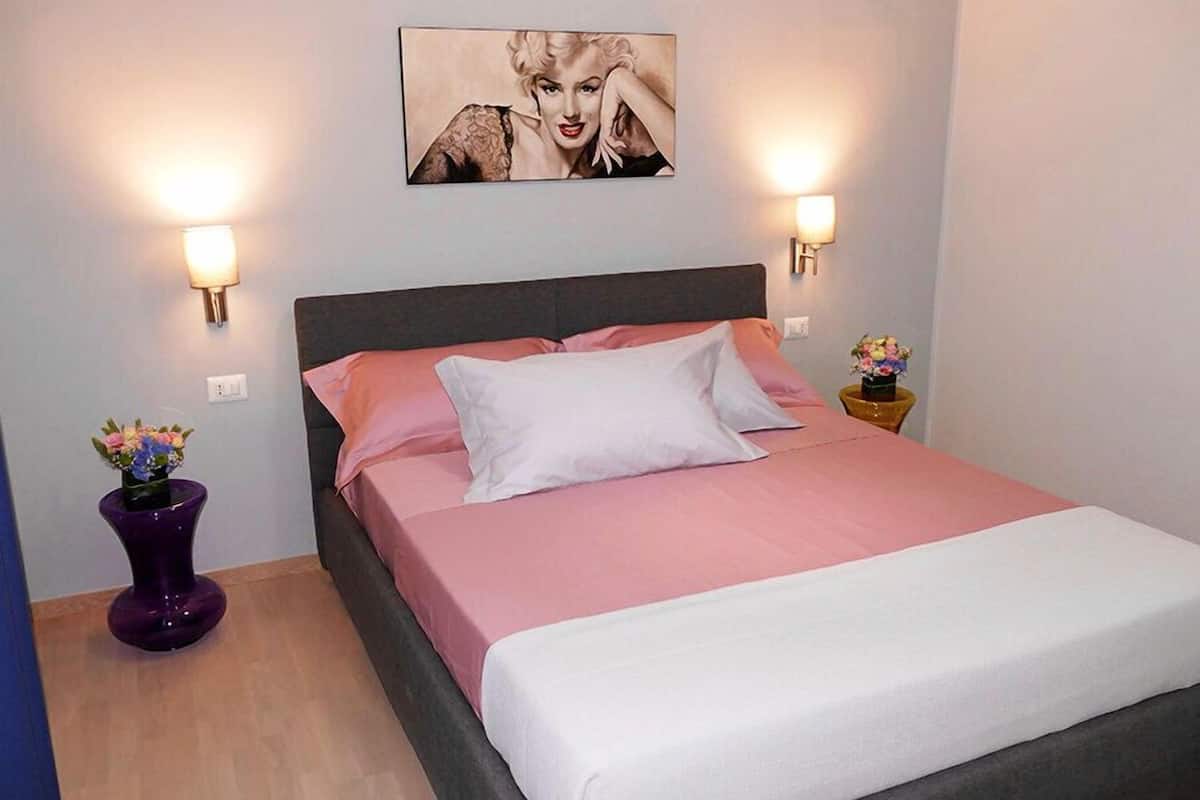 Ein Schlafzimmer mit einem Bett, zwei Wandleuchten und einem gerahmten Bild über dem Bett.