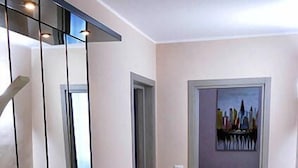 Een hal met een zwarte, reflecterende console tafel, een marmeren vloer en een deur die leidt naar een kamer met een bed en een schilderij aan de muur.