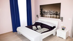 Een moderne slaapkamer met een bed, nachtkastje, wandlamp en een stadslandschap schilderij.