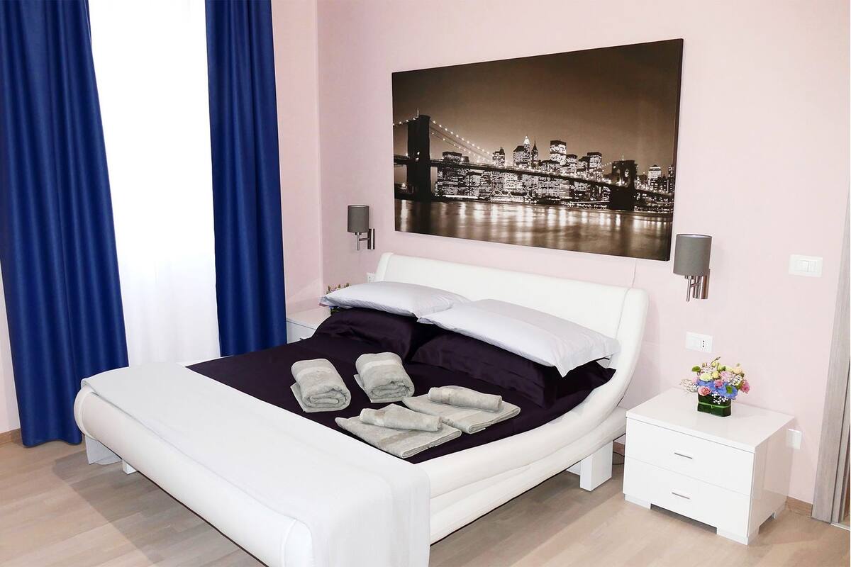 Ein modernes Schlafzimmer mit einem Bett, einem Nachttisch, einer Wandlampe und einem Stadtbild.
