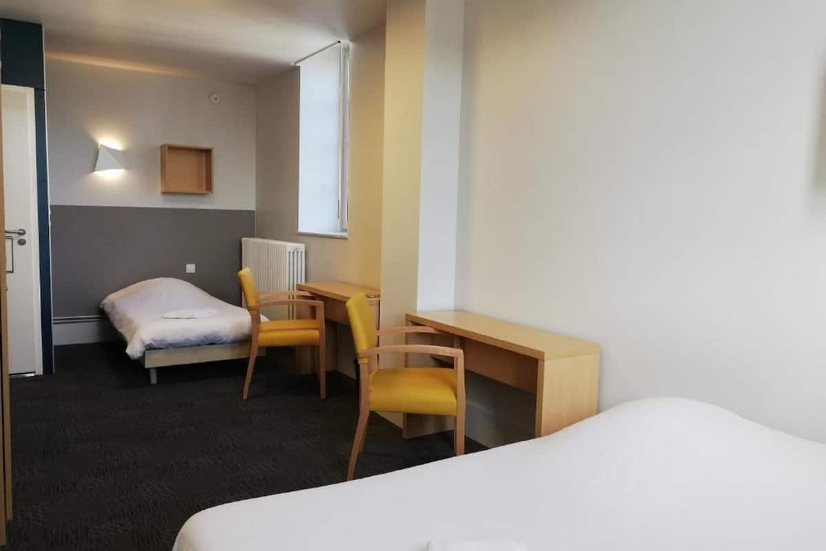 Una habitación de hotel con una cama, un escritorio, dos sillas, un radiador y una ventana.