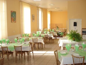 Uma área de refeições com várias mesas preparadas para hóspedes, com toalhas de mesa verdes e cadeiras.