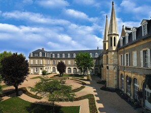 Un grand bâtiment historique doté d’une cour symétrique, avec une fontaine centrale et des jardins aménagés avec soin.