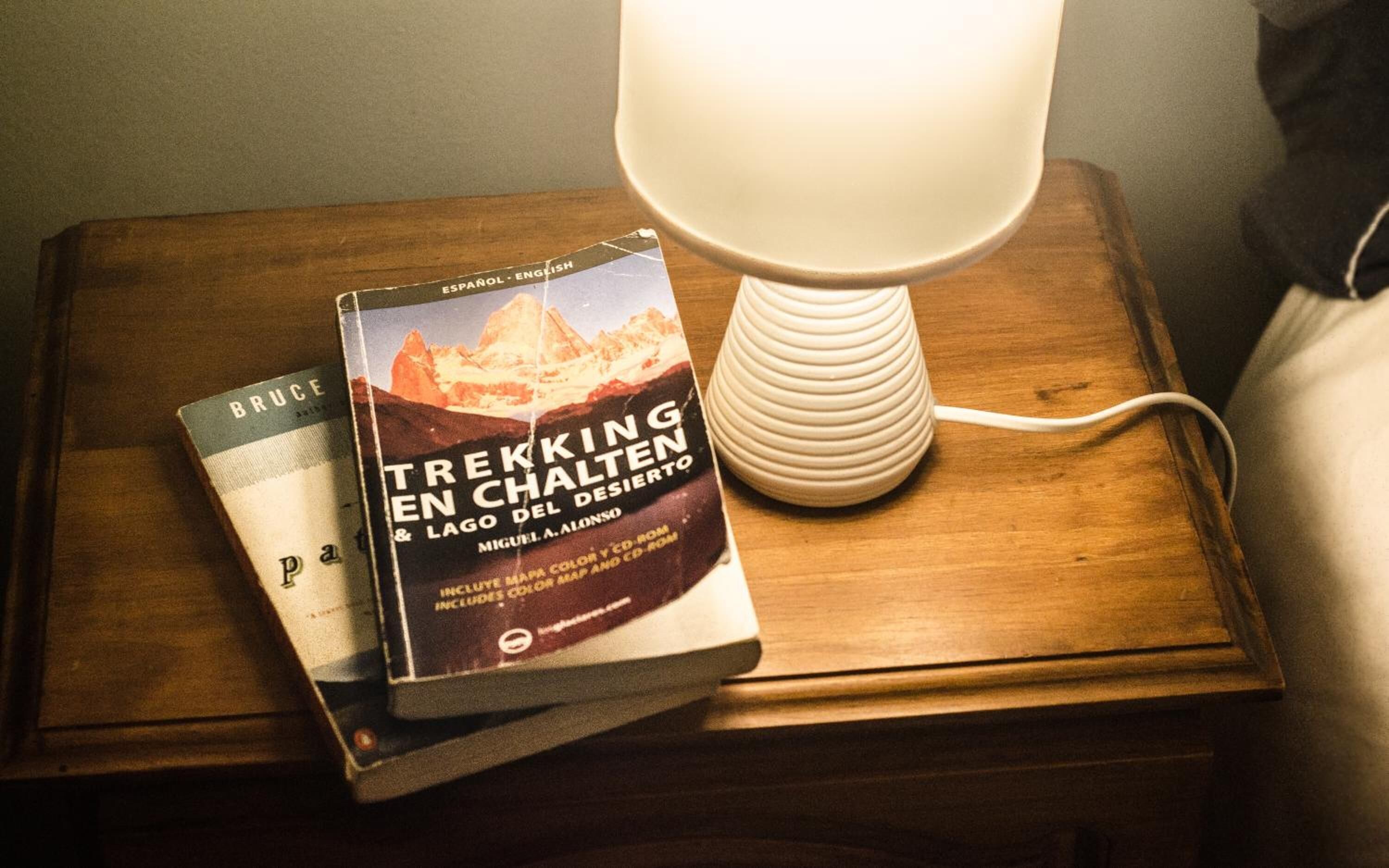 A stack of books on a wooden nightstand with a white lamp beside them.