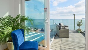 A balcony with a glass door, a blue chair, a wicker sofa, a potted plant, and a view of the sea. - Channel View Hotel (Paignton)