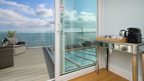 A balcony with a glass door, a wicker sofa, a small table with a coffee maker, and a view of the sea. - Channel View Hotel (Paignton)