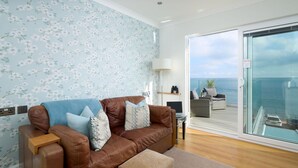 A modern living room with a brown leather sofa, a blue floral wallpaper, and a view of the sea through a glass door. - Channel View Hotel (Paignton)