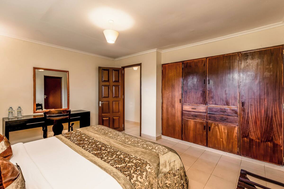A hotel room with a bed, a desk with a mirror, a wardrobe, and a door leading to another room.
