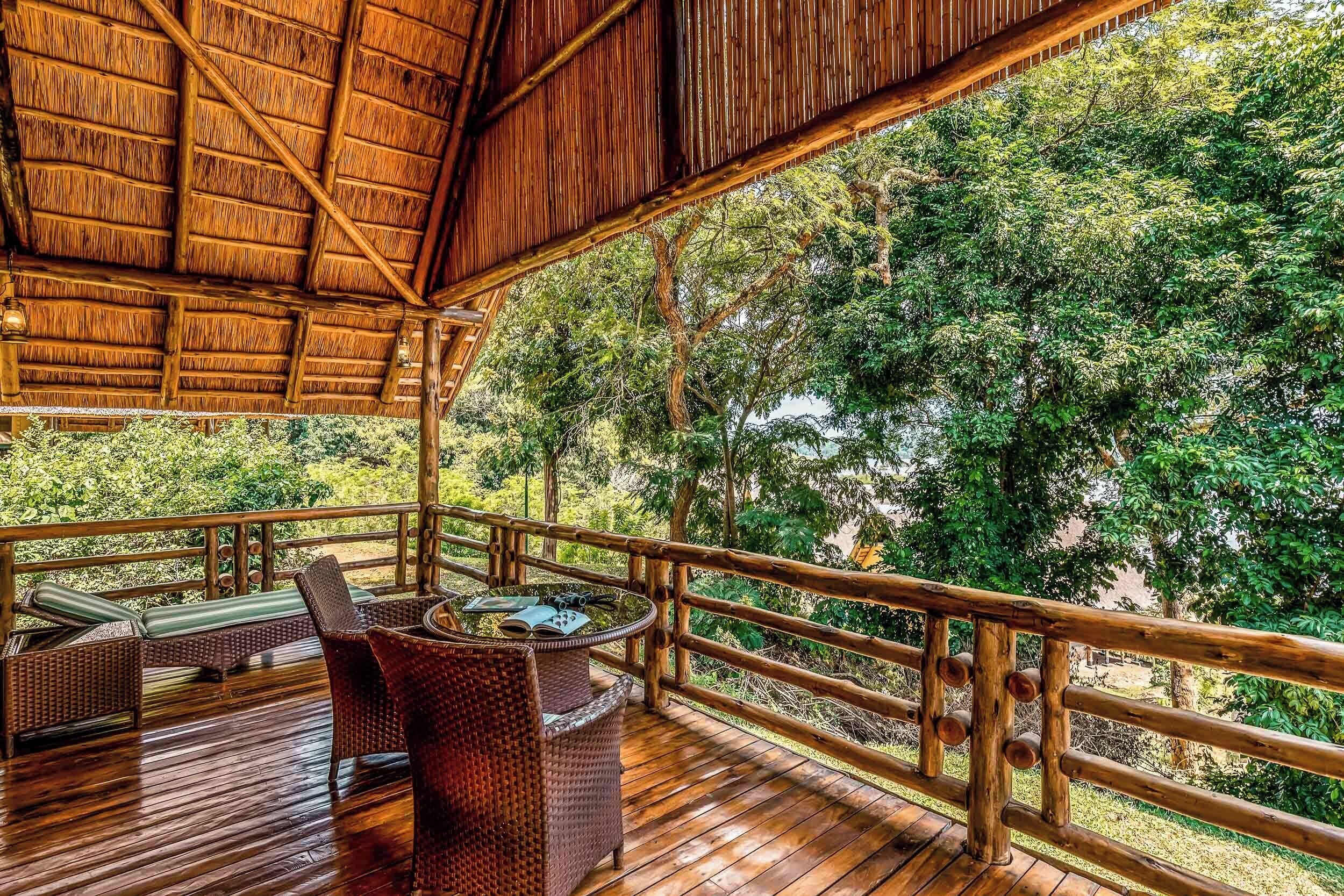 A wooden deck with wicker furniture and a thatched roof, overlooking a lush forest.