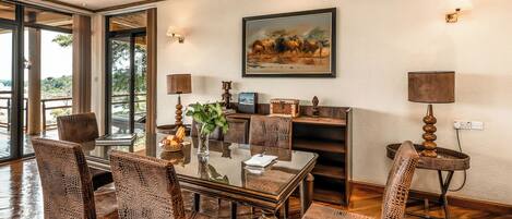 Un coin repas avec une table en verre, des chaises en osier et un tableau représentant des éléphants accroché au mur.