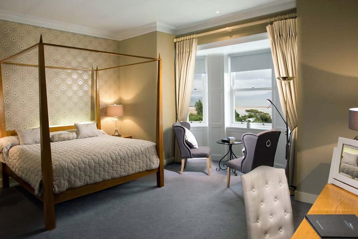 Un lit à baldaquin, un bureau avec une lampe, une chaise et une vue sur l’extérieur par une fenêtre.