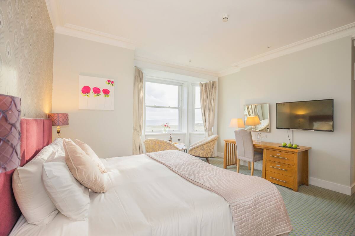 Une chambre d’hôtel avec un lit, un bureau, une chaise, une télévision et une fenêtre avec des rideaux.