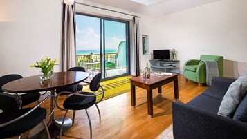 Una sala de estar moderna con comedor, un sofá verde, un televisor y un balcón con vista al mar.