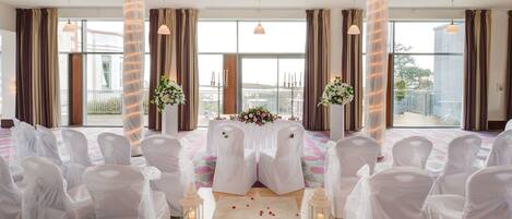A wedding ceremony setup with white chairs, a floral arrangement, and candles.