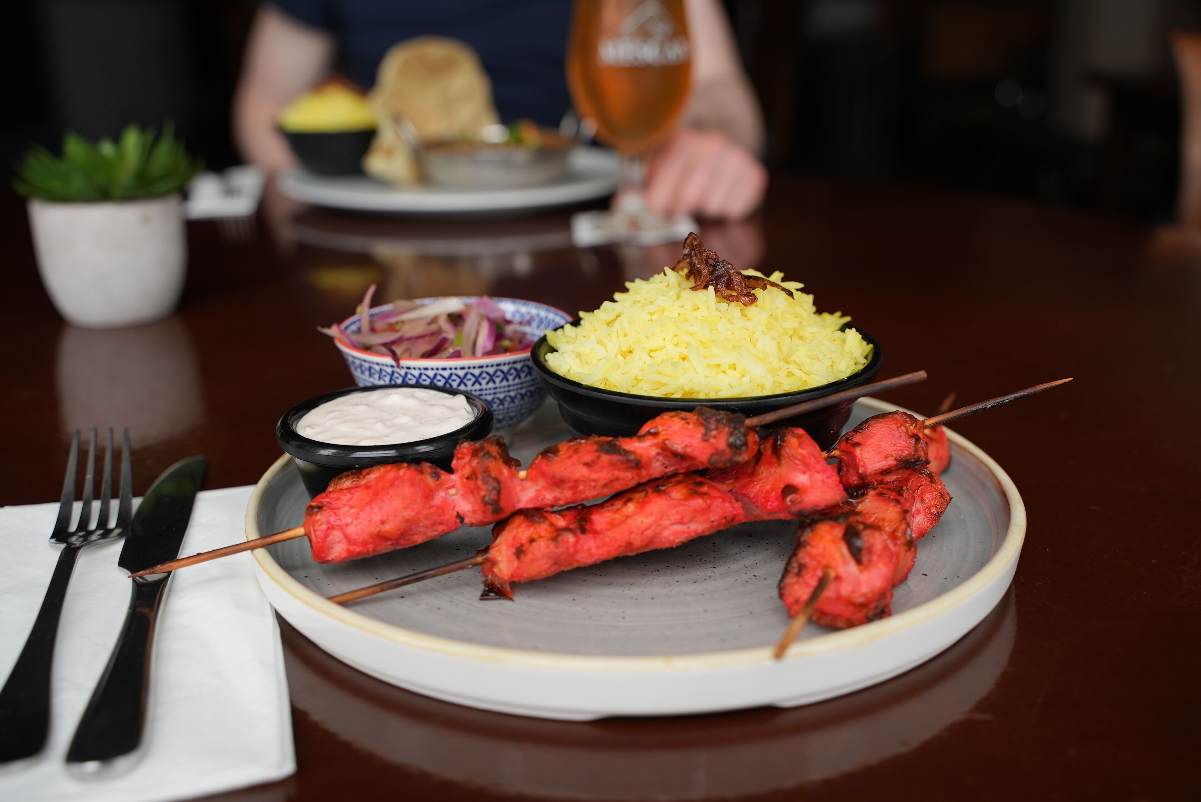 A plate with skewered meat, rice, and a small bowl of sauce.
