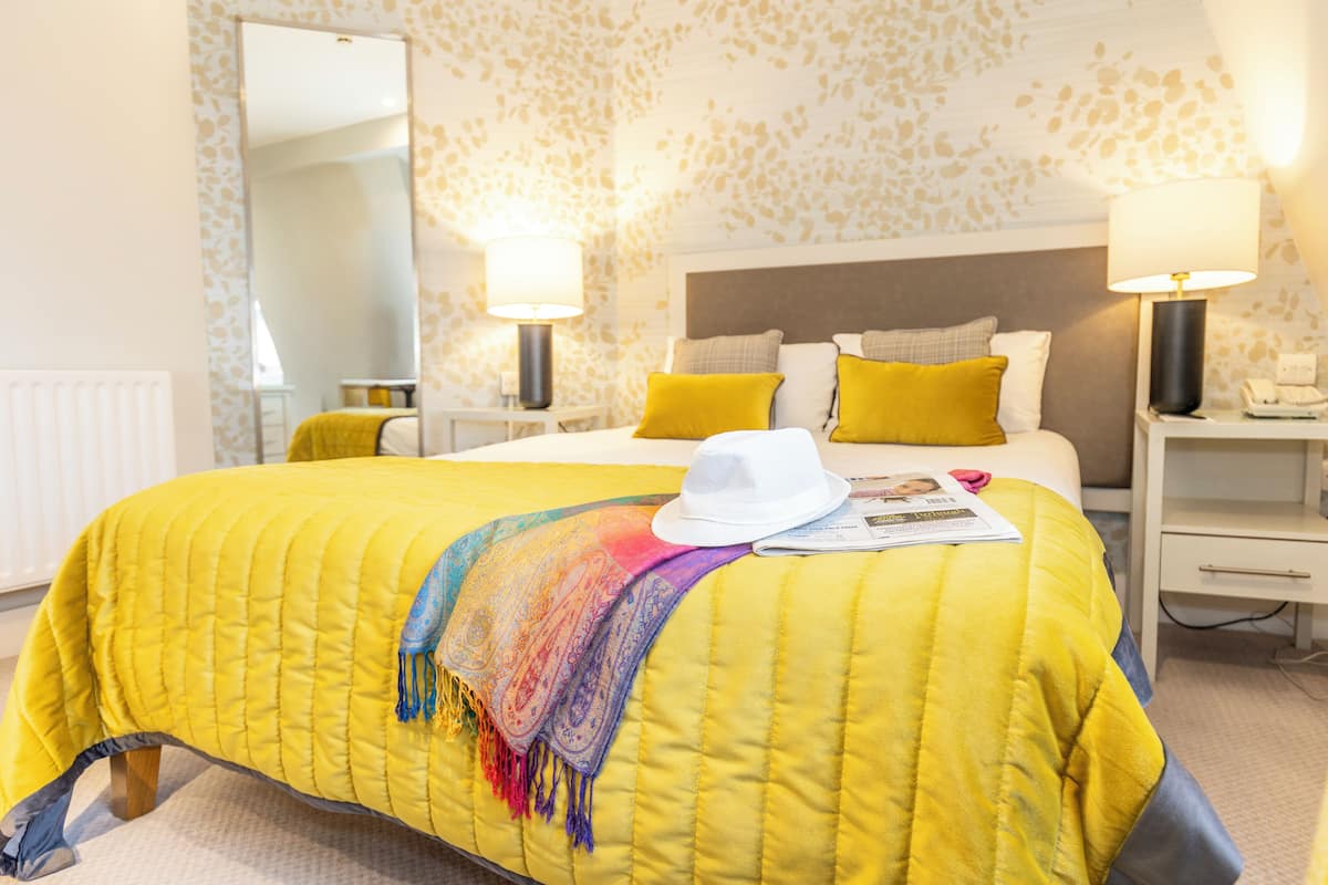 Une chambre d’hôtel avec un grand lit, deux tables de chevet, une commode, un miroir et une fenêtre.