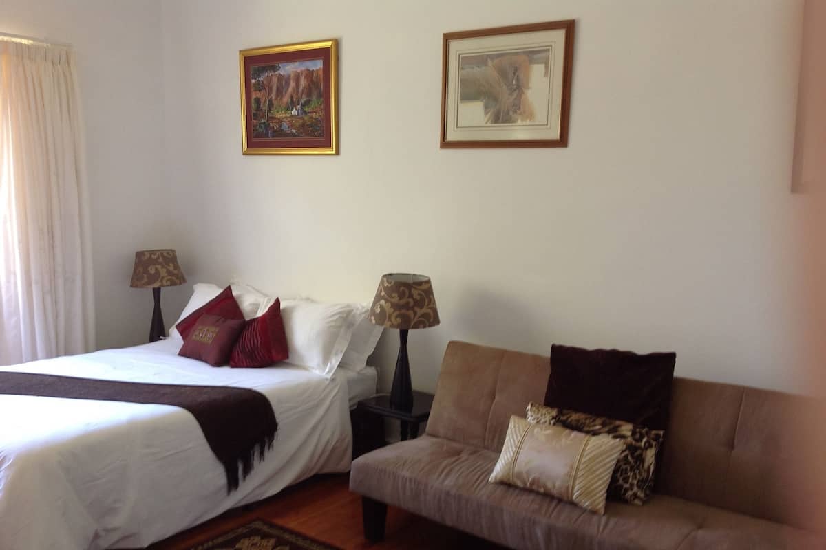 A hotel room with a bed, a sofa, two lamps, and two framed pictures on the wall.