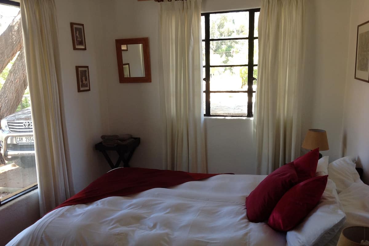 A bedroom with a bed, pillows, a nightstand, a lamp, and a window with curtains.