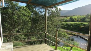 A wooden deck with a railing overlooking a river and greenery. - Swaynekloof Farm (Bot River)