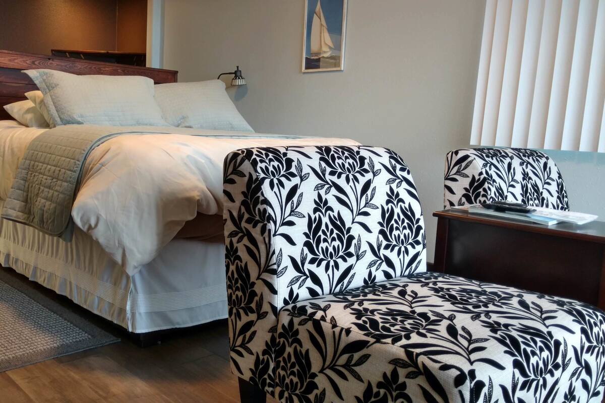A bedroom with a bed, a chair, a nightstand, a lamp, and a painting on the wall.