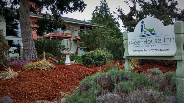 A sign for the GreenHouse Inn by the Bay, surrounded by landscaped garden beds and a variety of plants. - GreenHouse Inn by the Bay (Sequim)