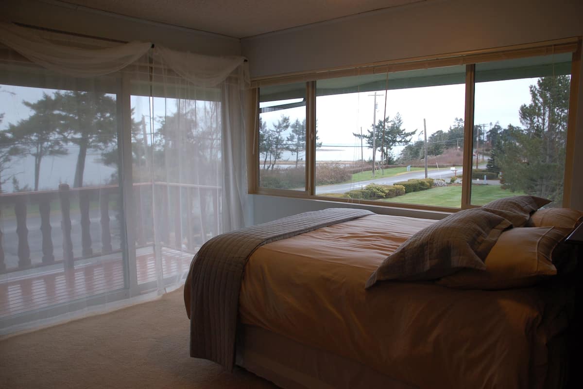 A bedroom with a large window, a bed, and a view of a deck and trees.