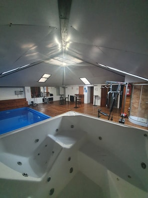 A room with a large window, a wooden floor, a white bathtub, and a small pool.