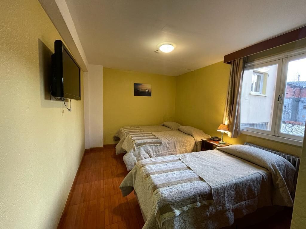 A room with two beds, a television, a window with curtains, and a picture on the wall.