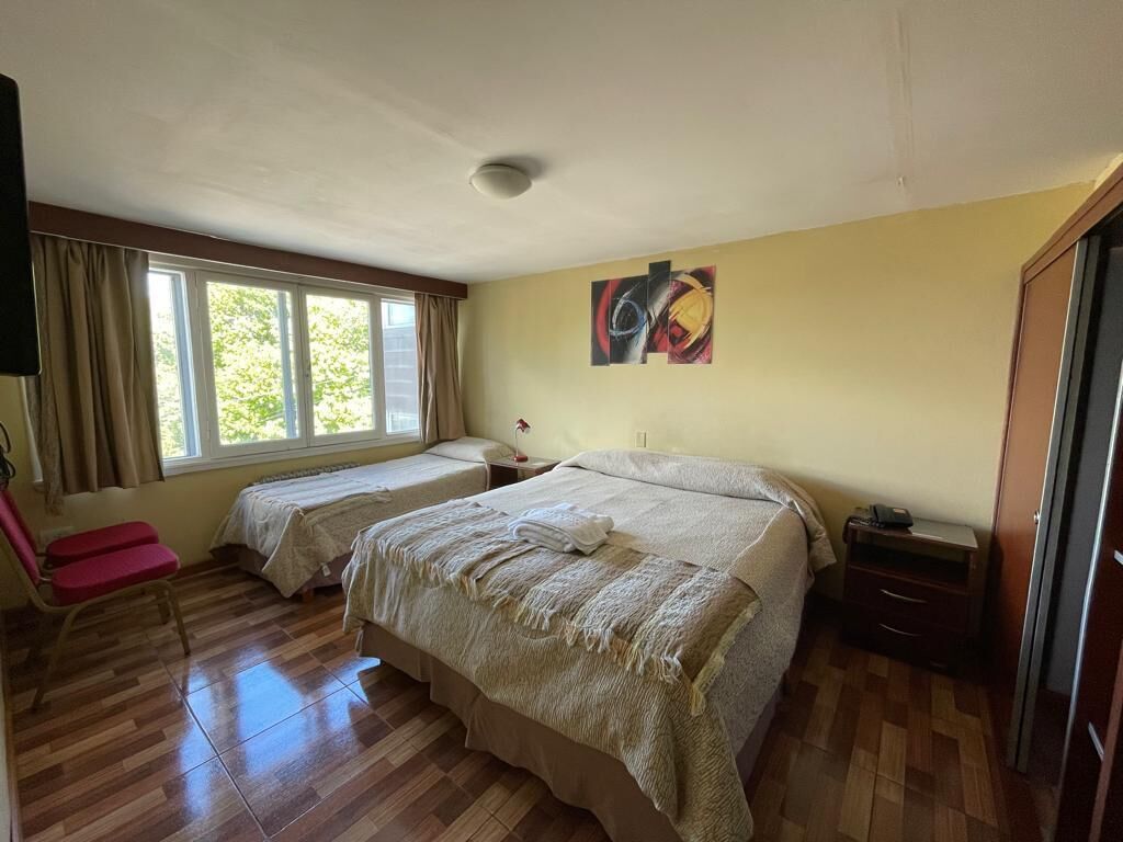 A room with two beds, a chair, a desk, and a window with curtains.