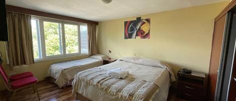 A room with two beds, a chair, a desk, and a window with curtains.