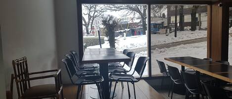 A restaurant with a large window view of a snowy outdoor area, including a tree and parked vehicles.