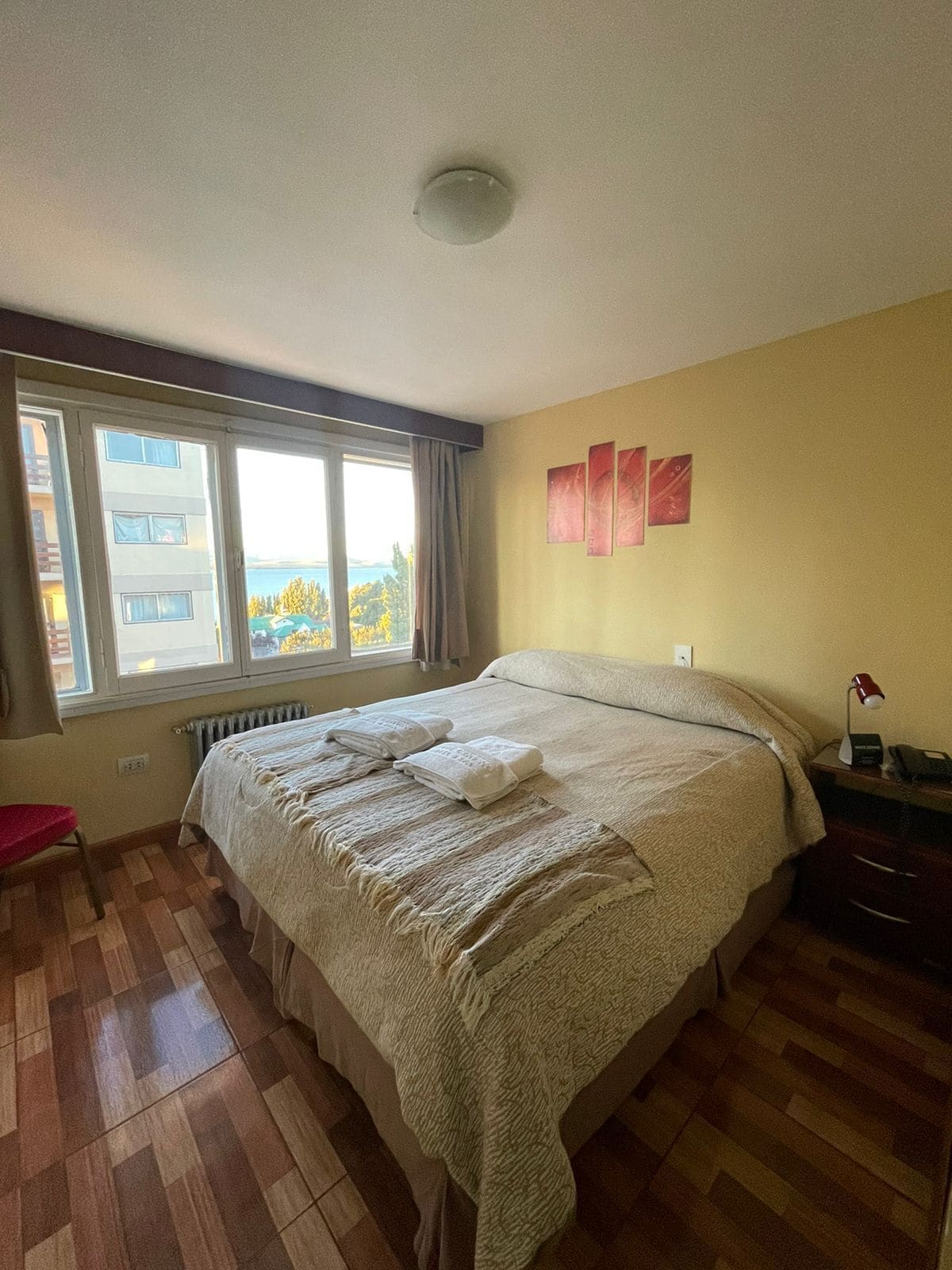 A bedroom with a large bed, a window, a radiator, and a red chair.