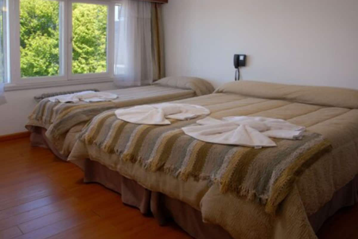 Camera d'albergo con due letti, una finestra con tende e un telefono attaccato al muro.
