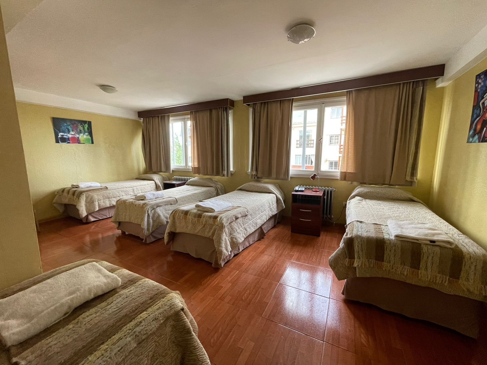 Quarto de hotel com quatro camas, um radiador e uma janela com cortinas.
