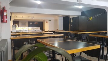 Un comedor con mesas y sillas, un extintor, una cafetera y una pizarra con un mensaje de bienvenida.