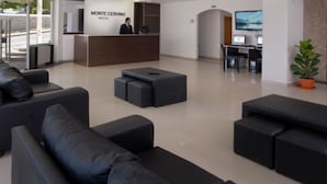 A hotel lobby with a reception desk, black sofas, and a TV screen. - Hotel Monte Cervino (San Carlos de Bariloche)