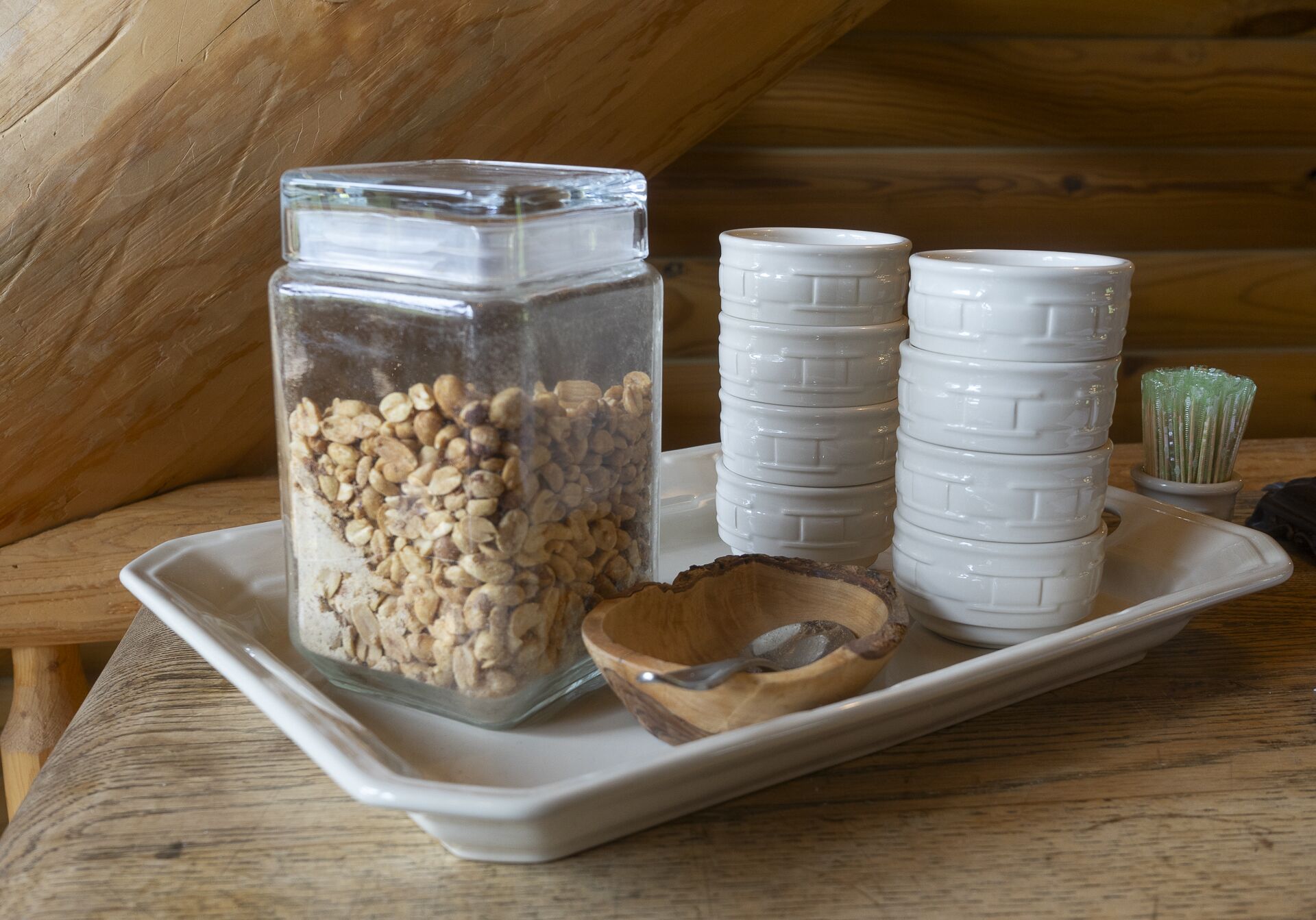 A tray with a glass jar of oats, a wooden bowl, and stacked white ceramic cups.