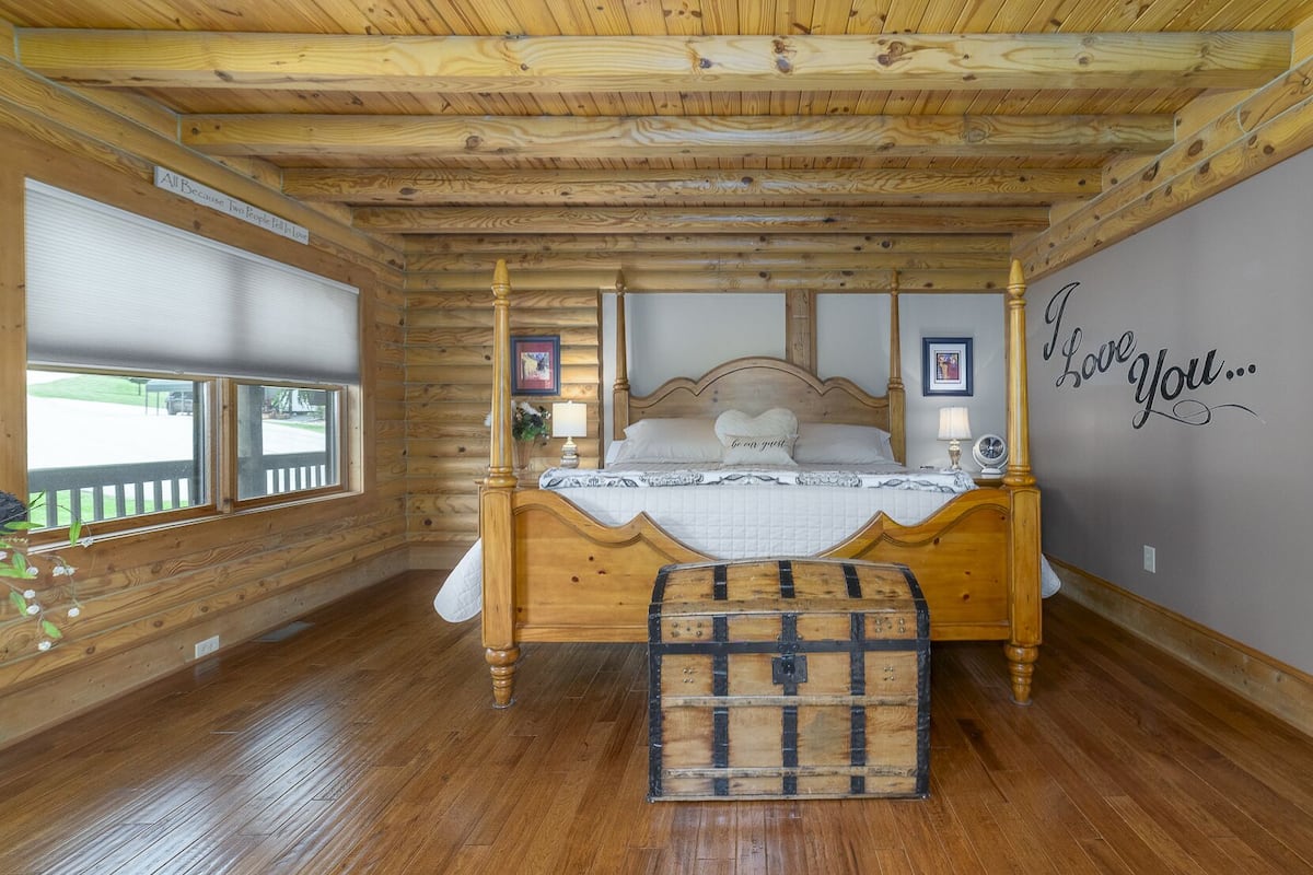 A wooden cabin bedroom with a four-poster bed, a bench, and a wall with a 'Love You...' message.