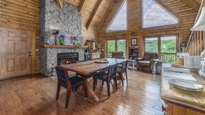 Una cabaña espaciosa con chimenea de piedra, mesa de comedor de madera y ventanas amplias que ofrecen vistas panorámicas.