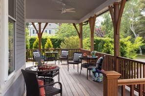 Une terrasse extérieure couverte, aménagée avec des meubles en osier, un ventilateur de plafond et offrant une vue sur une maison et la verdure environnante.