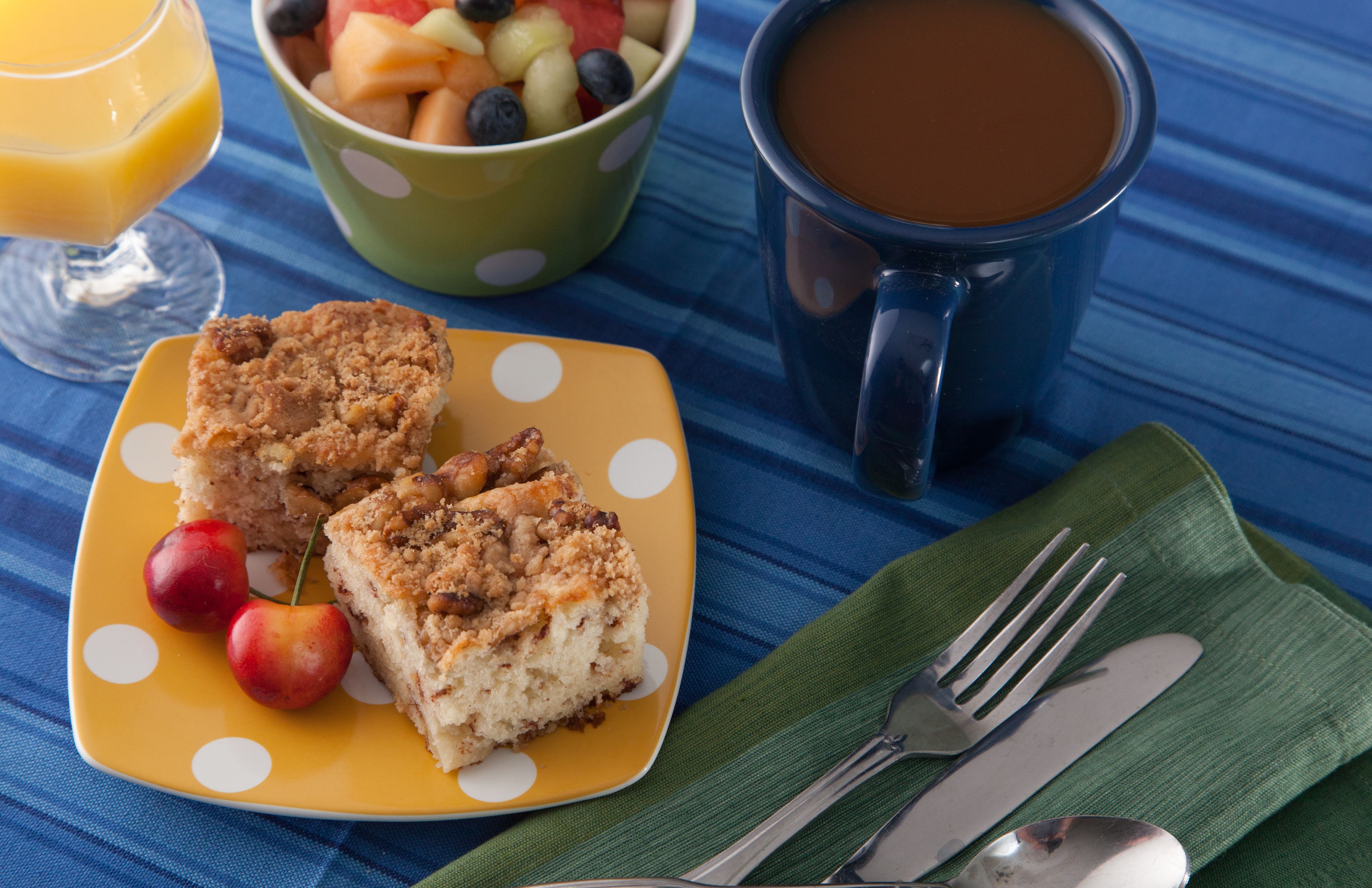 A breakfast setting with a plate of food, a mug of coffee, and a glass of orange juice on a blue tablecloth.
