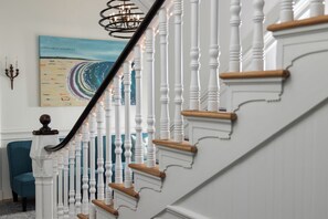 Un escalier avec des balustrades blanches et des rampes en bois, menant à un palier où se trouvent une chaise bleue et un tableau.