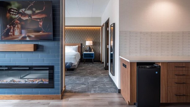 A modern hotel room with a fireplace, a bed, a nightstand, and a kitchen area. - Grand Casino Mille Lacs Hotel (Onamia)