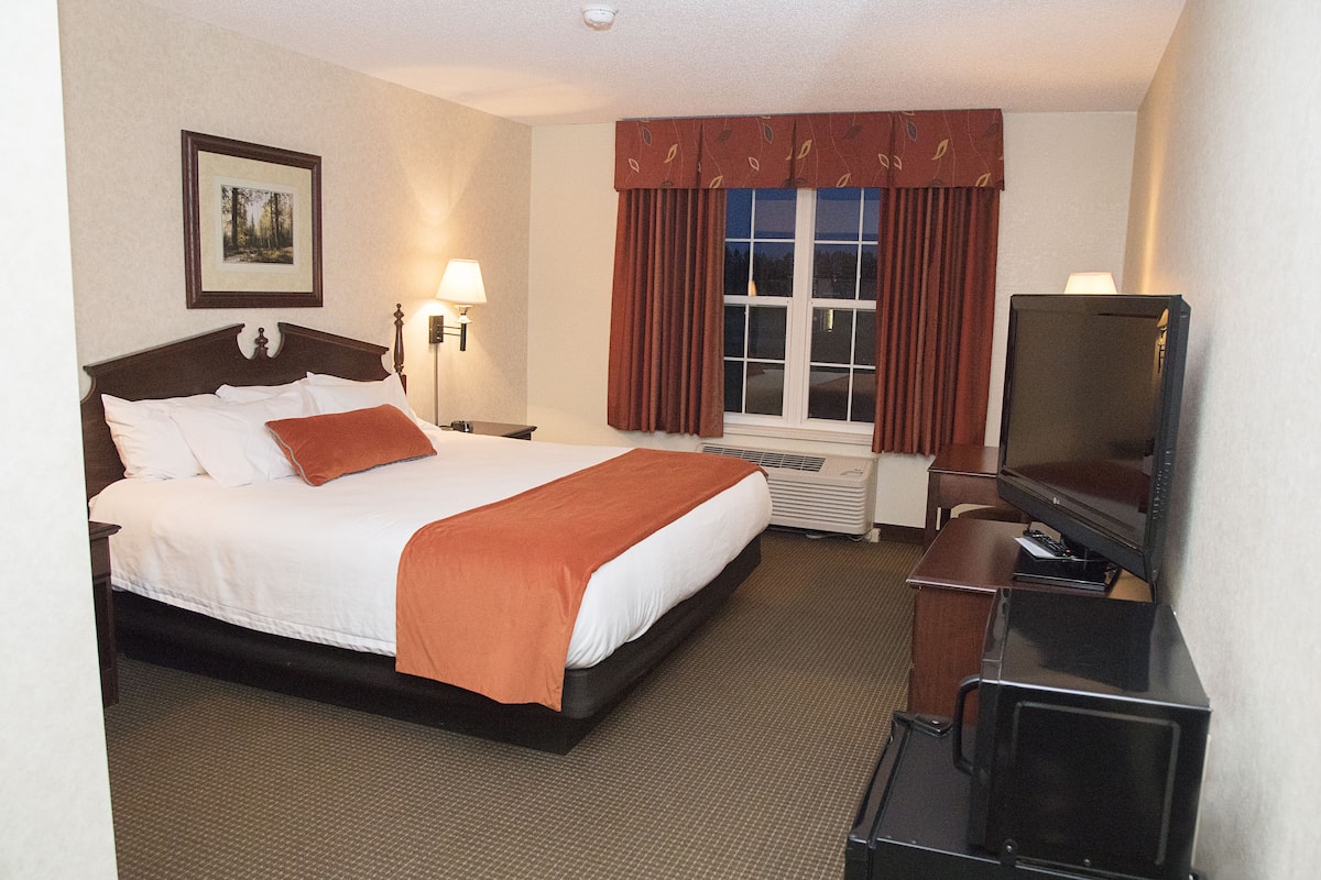 Ein Hotelzimmer mit einem Bett, einem Fernseher, einem Schreibtisch und einem Fenster mit Vorhängen.