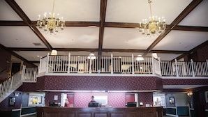 Un'hall d'albergo con una reception in legno, un lampadario e un balcone con ringhiera, oltre a una scala.