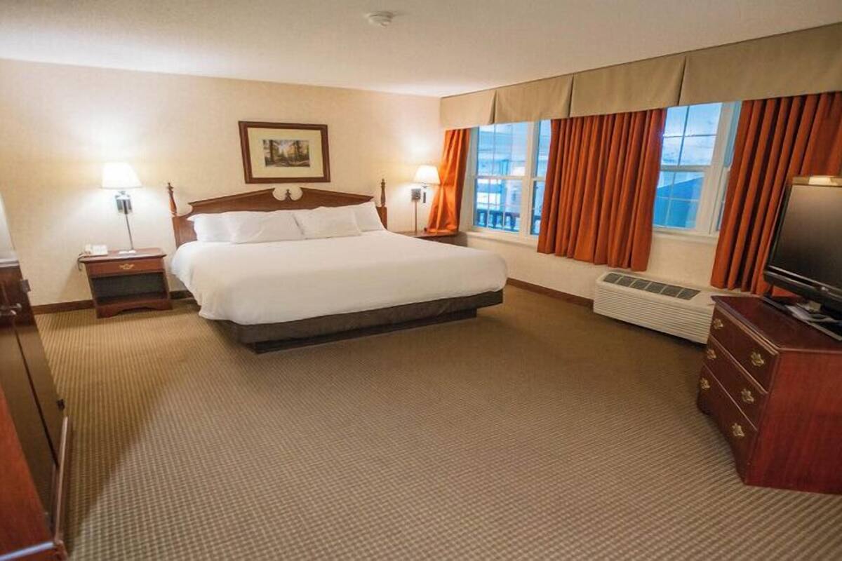 Ein Hotelzimmer mit einem großen Bett, einem Flachbildfernseher, einem Schminktisch, einem Heizkörper und einem Fenster mit Vorhängen.