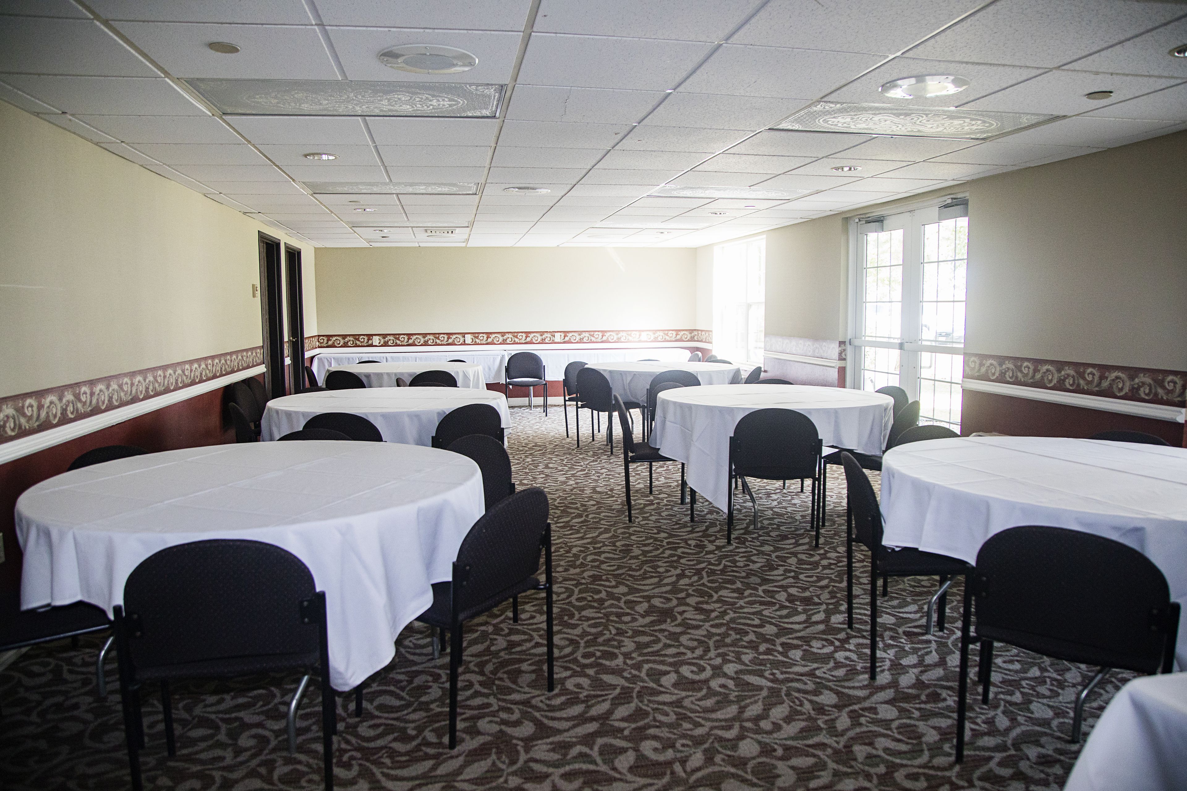 A conference room with multiple round tables, black chairs, and patterned carpet.