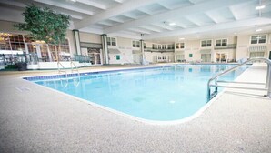 Una piscina interna con acqua cristallina, circondata da un pavimento piastrellato e una scala per la piscina in metallo.