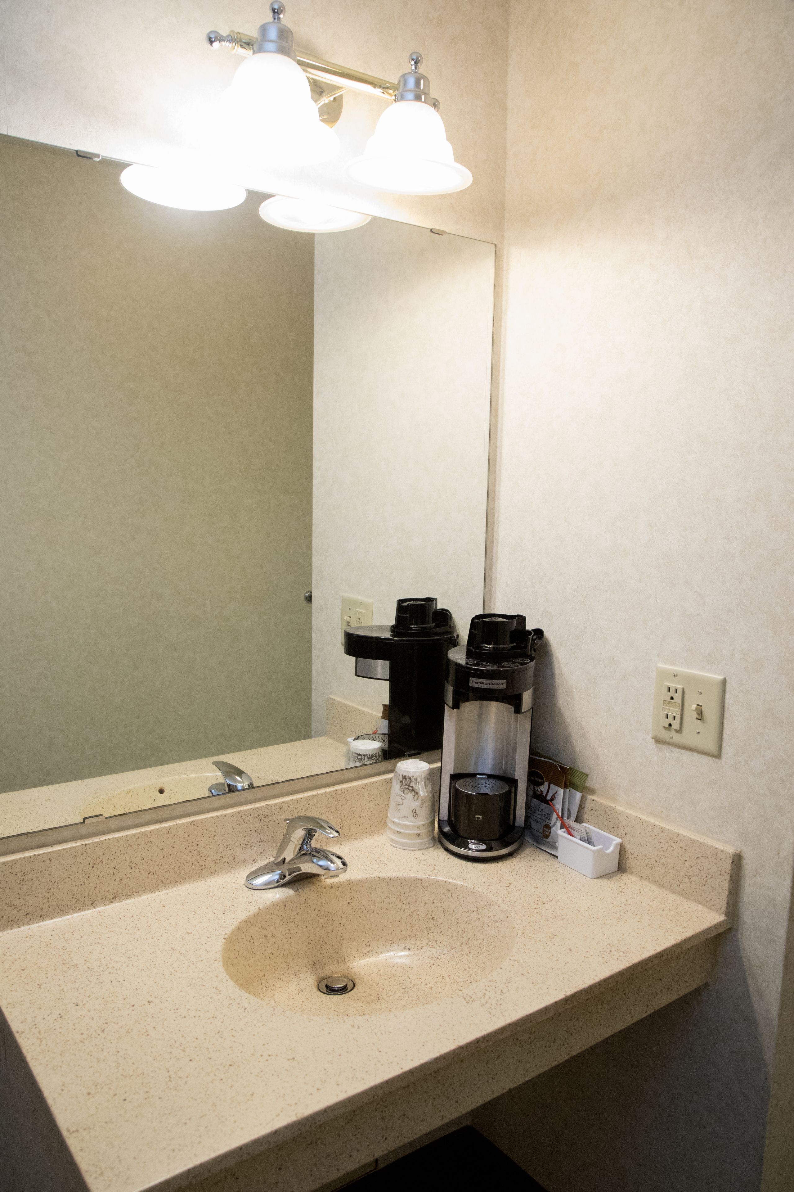 A bathroom with a sink, two coffee makers, and a mirror.